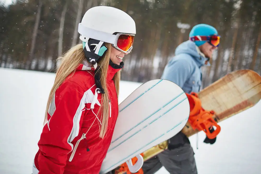 Man and woman carrying snowboards